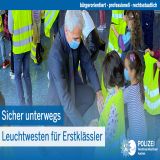 Polizeipräsident Dirk Weinspach verteilt Leuchtwesten an Erstklässlerinnen und Erstklässler.