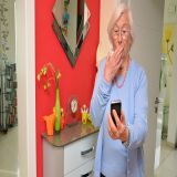 Eine Seniorin mit erschrockenem Blick auf das Telefon in ihrer Hand.
