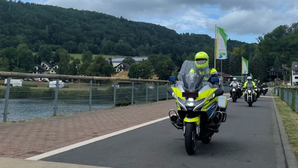 Mehrere Motorradfahrer überqueren eine Brücke in Rurberg in der Eifel. Geführt wird die Gruppe von einem Polizei-Motorrad.